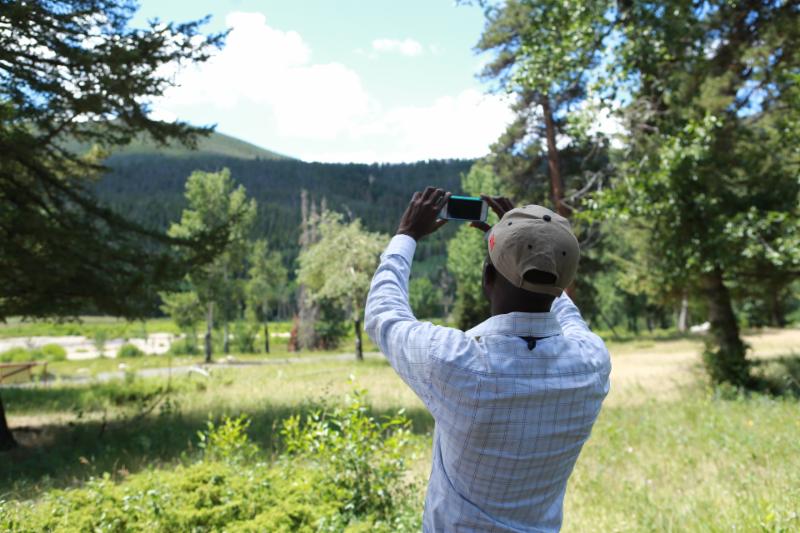 Man wearing hat photographing clouds with cell phone.