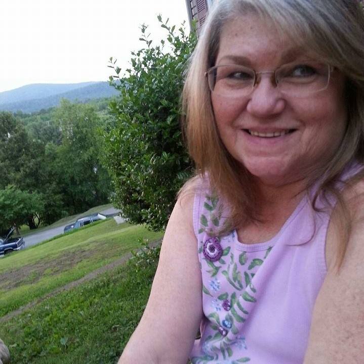 A woman in glasses and a purple shirt smiles at the camera.