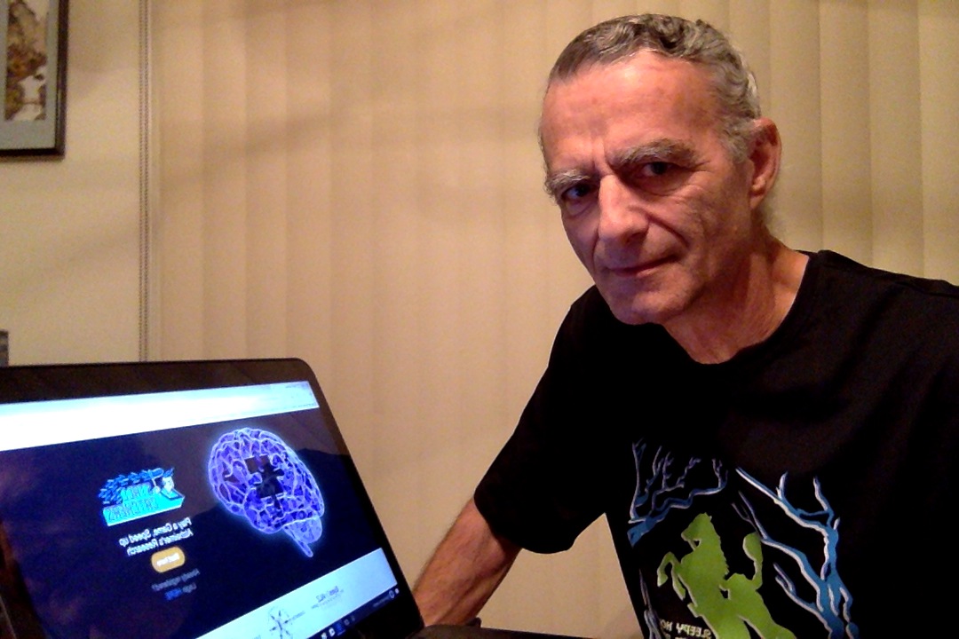 A man in a black t-shirt sits at a laptop.