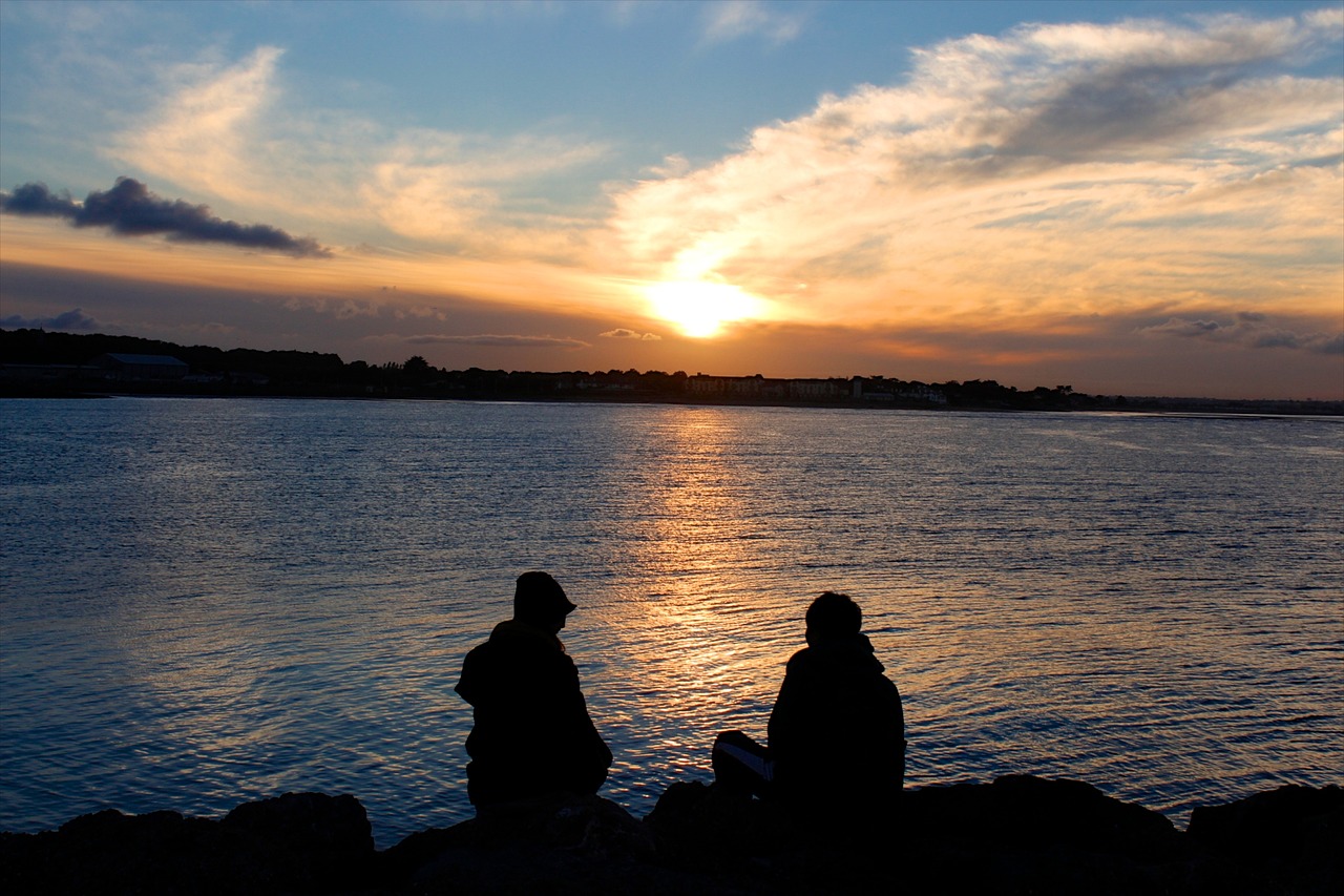Silhouette of a couple sitting on the shore, watching a sunset
