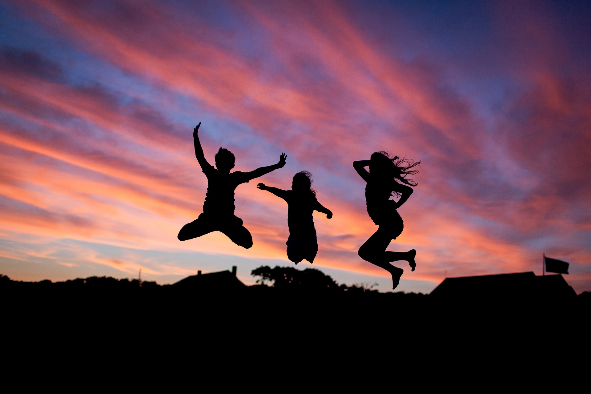 Silhouette of three people jumping happily in front of purple and blue sunset