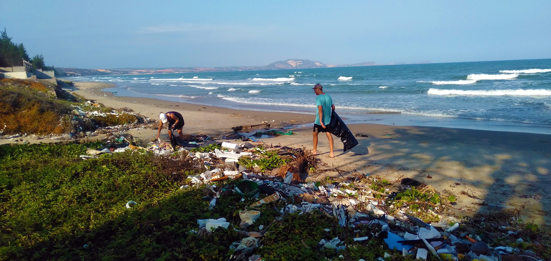 Photograph of litter-strewn beach, with two people picking up trash