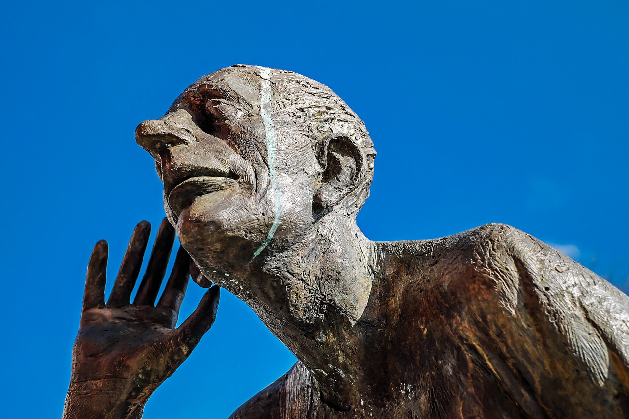 Photo of rock sculpture of man's head with hand held up to ear as if listening
