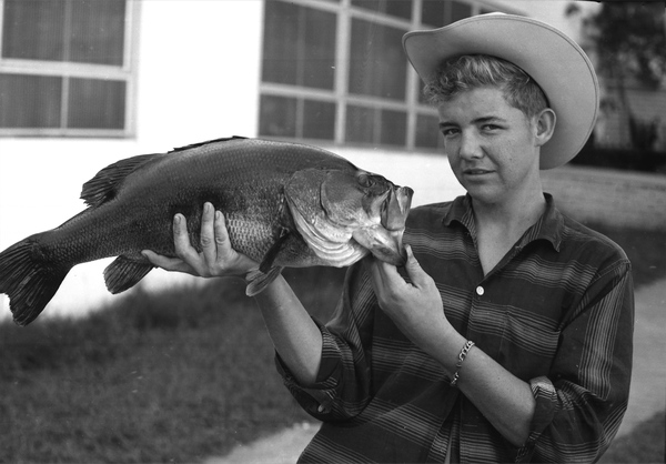 Old black and white photo of a boy holding a largemouth bass.