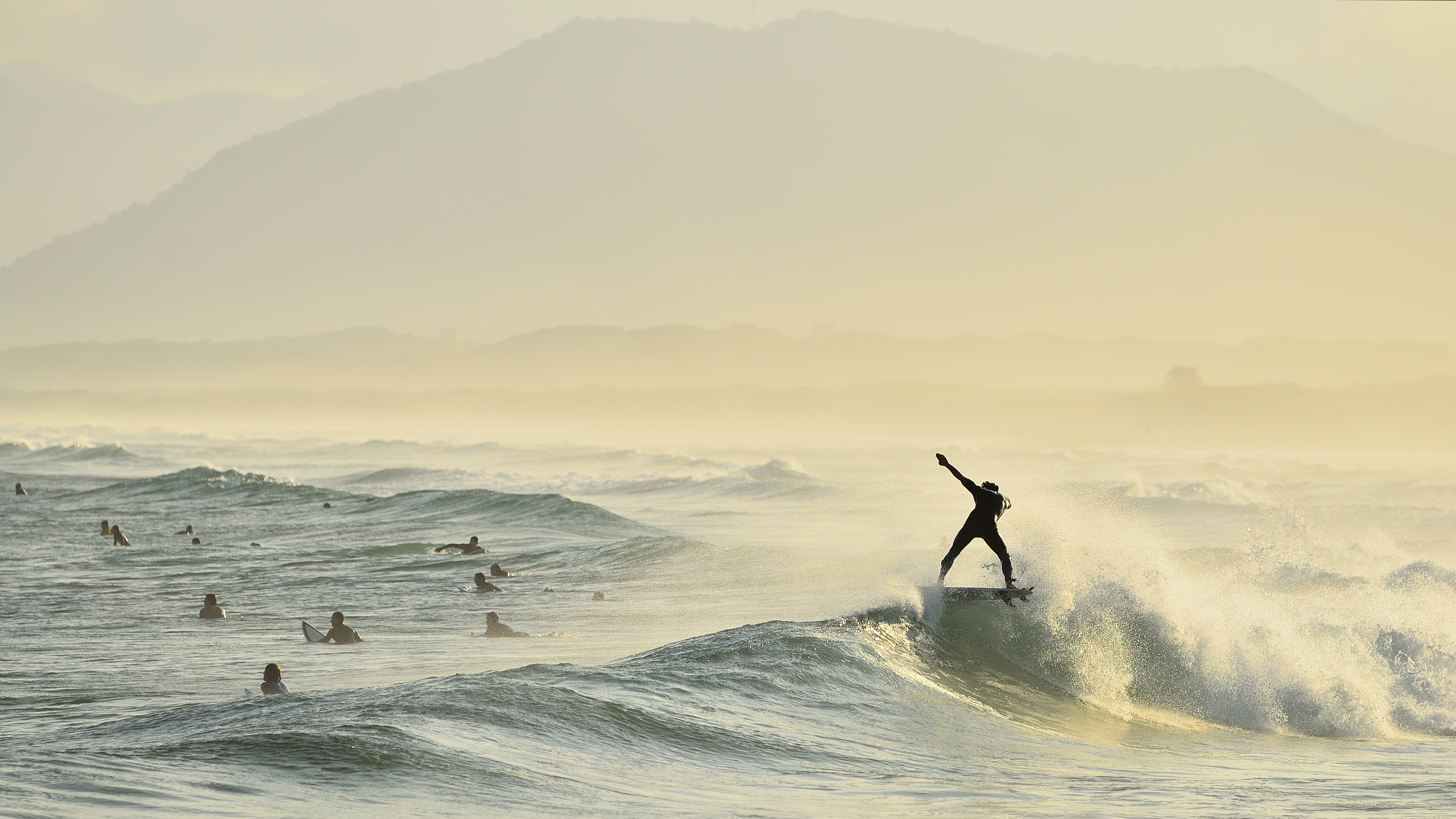 A panorama of surfers on a misty beach, with one silhouetted