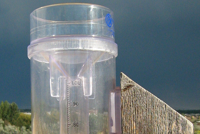 A clear plastic rain gauge against a dark grey sky.