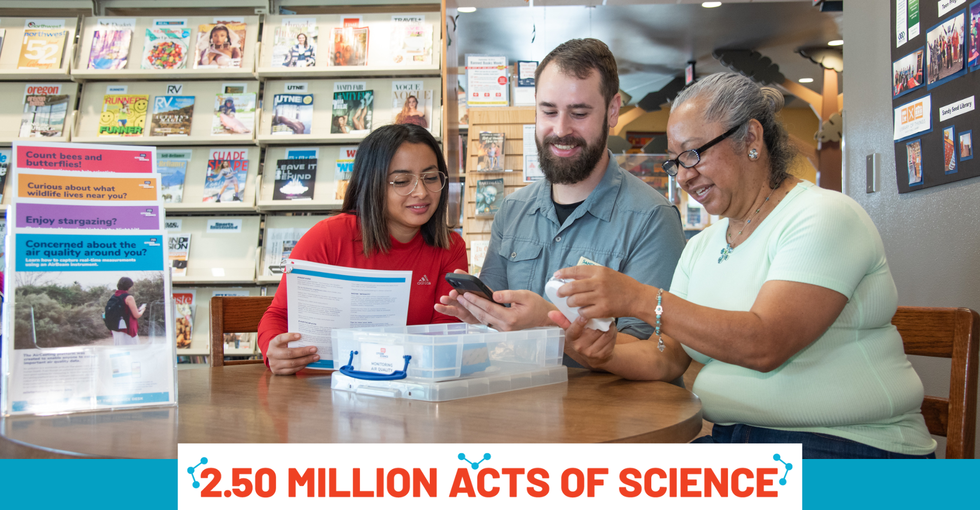 Three library patrons sitting in front of a citizen science kit. Kit is open and patrons are viewing the materials inside.