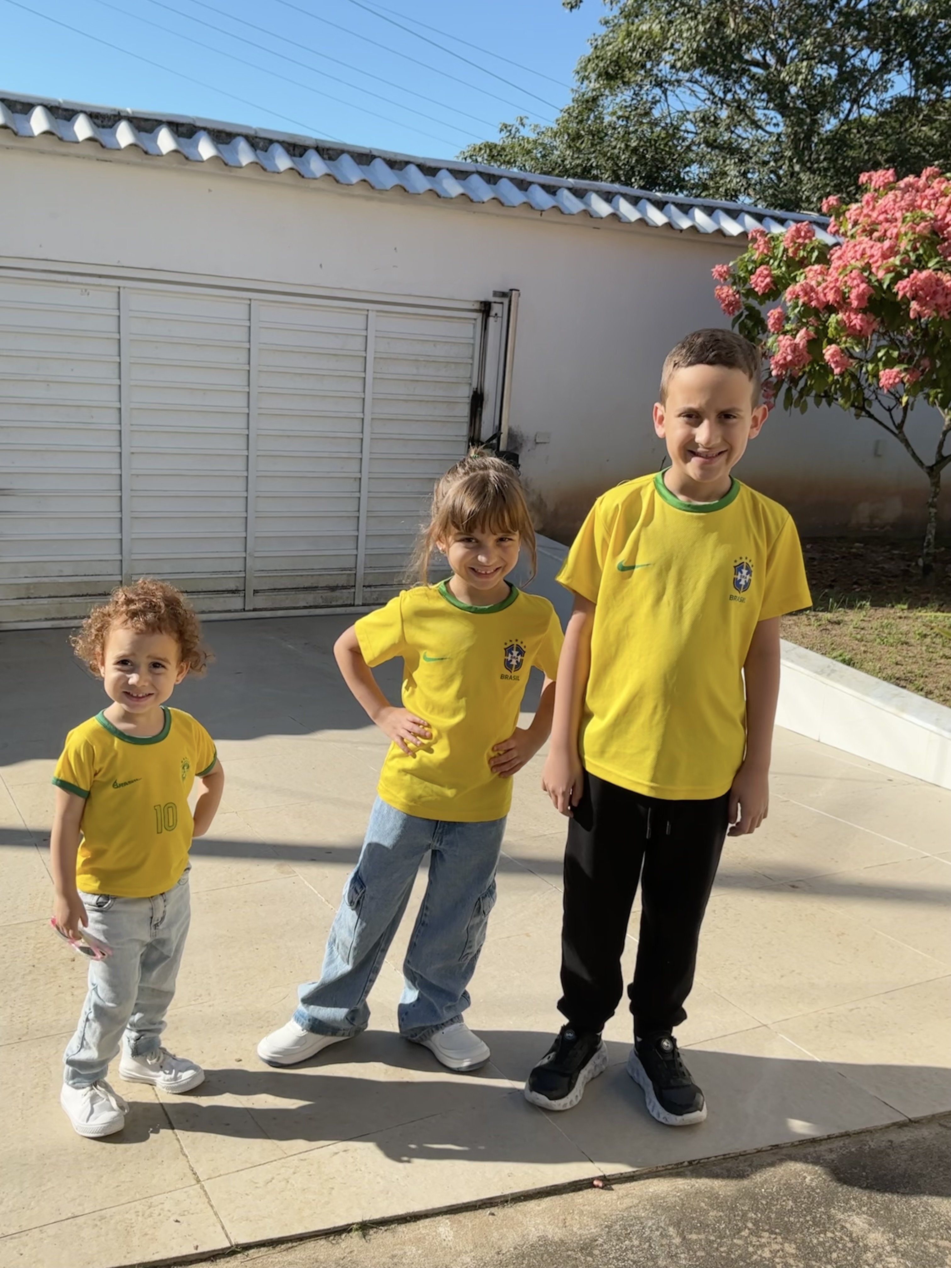 The young co-conceptualizers Sandeji Lorenzo (8) and Maria Clara (6), accompanied by volunteer toddler Emília Valentina (2), united in their backyard in Igarassu, Pernambuco, Brazil, wearing the Brazilian national colors.